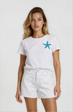 Woman wearing a white t-shirt with a blue starfish design and white shorts on a plain background