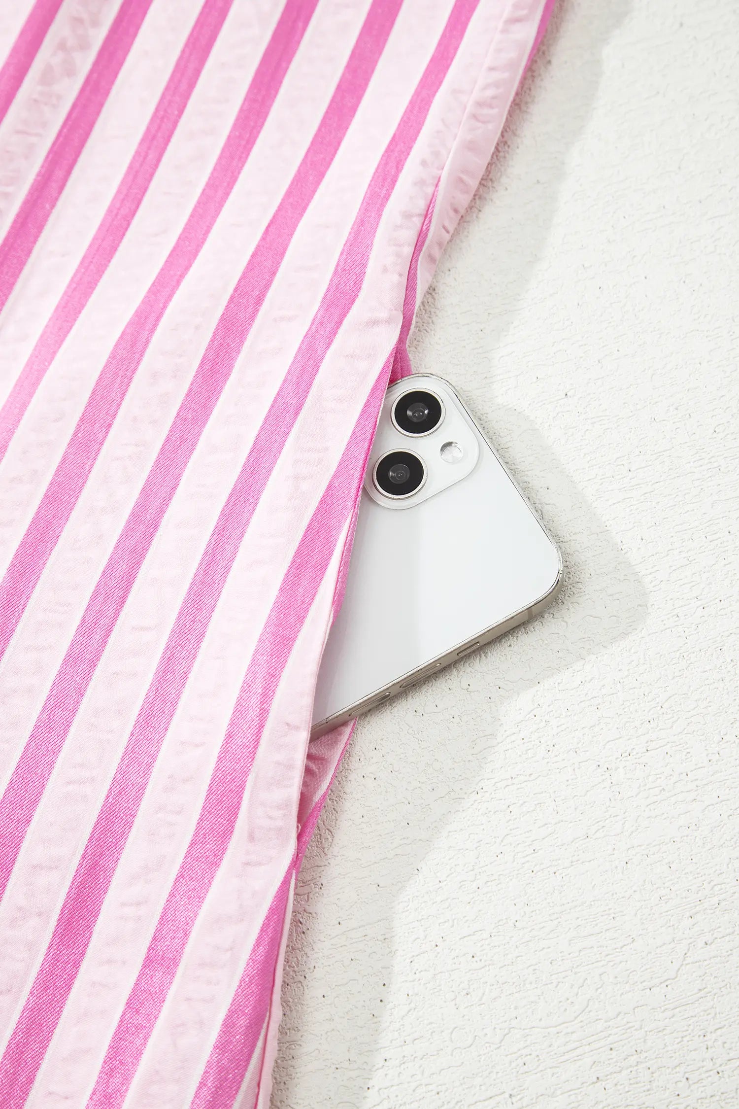 Pink and white striped fabric, likely a bed sheet or duvet cover, partially pulled away to reveal a white smartphone underneath on a textured white surface.