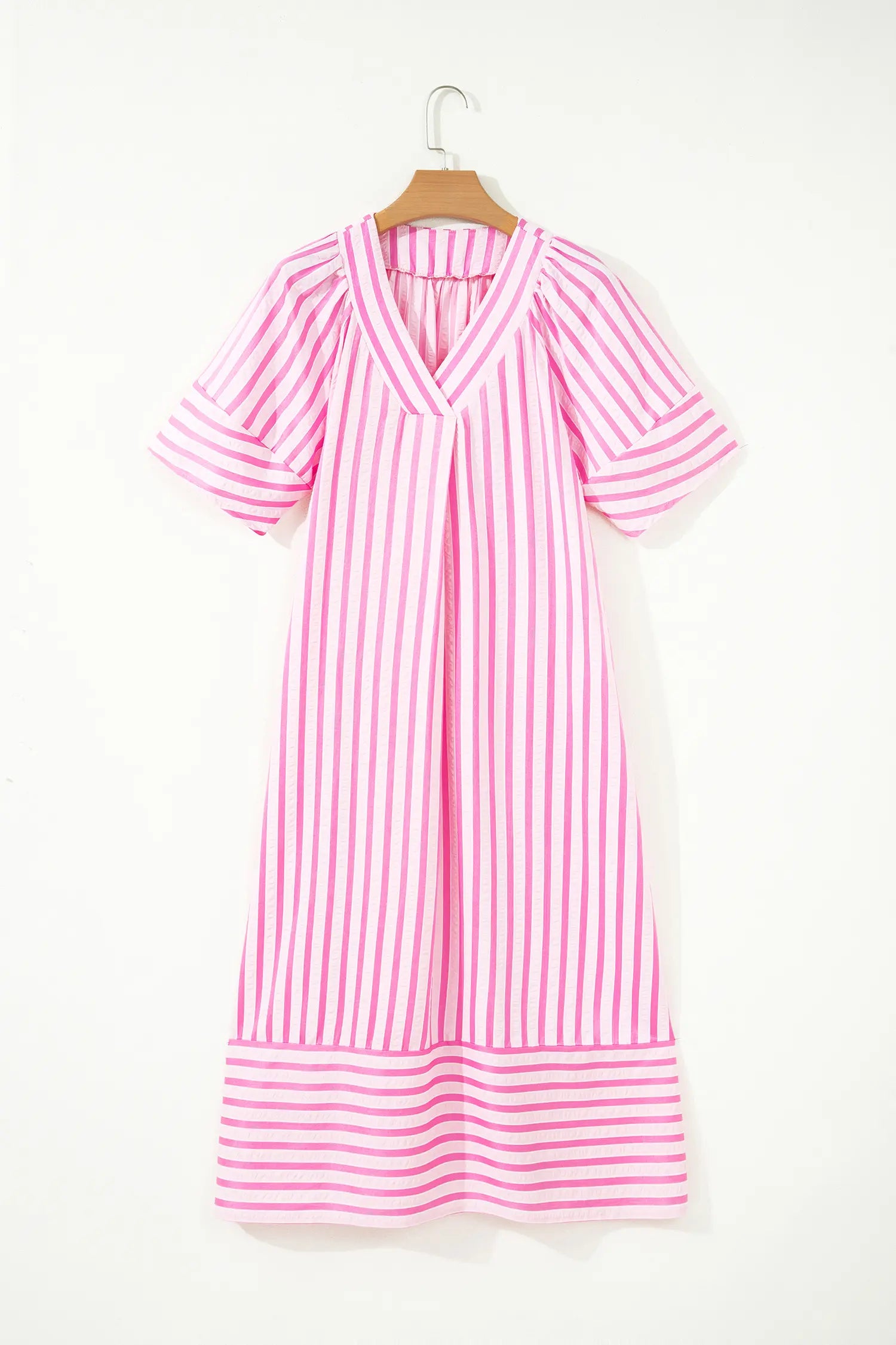 A pink and white vertically striped short-sleeve dress hanging on a wooden hanger against a plain white wall.