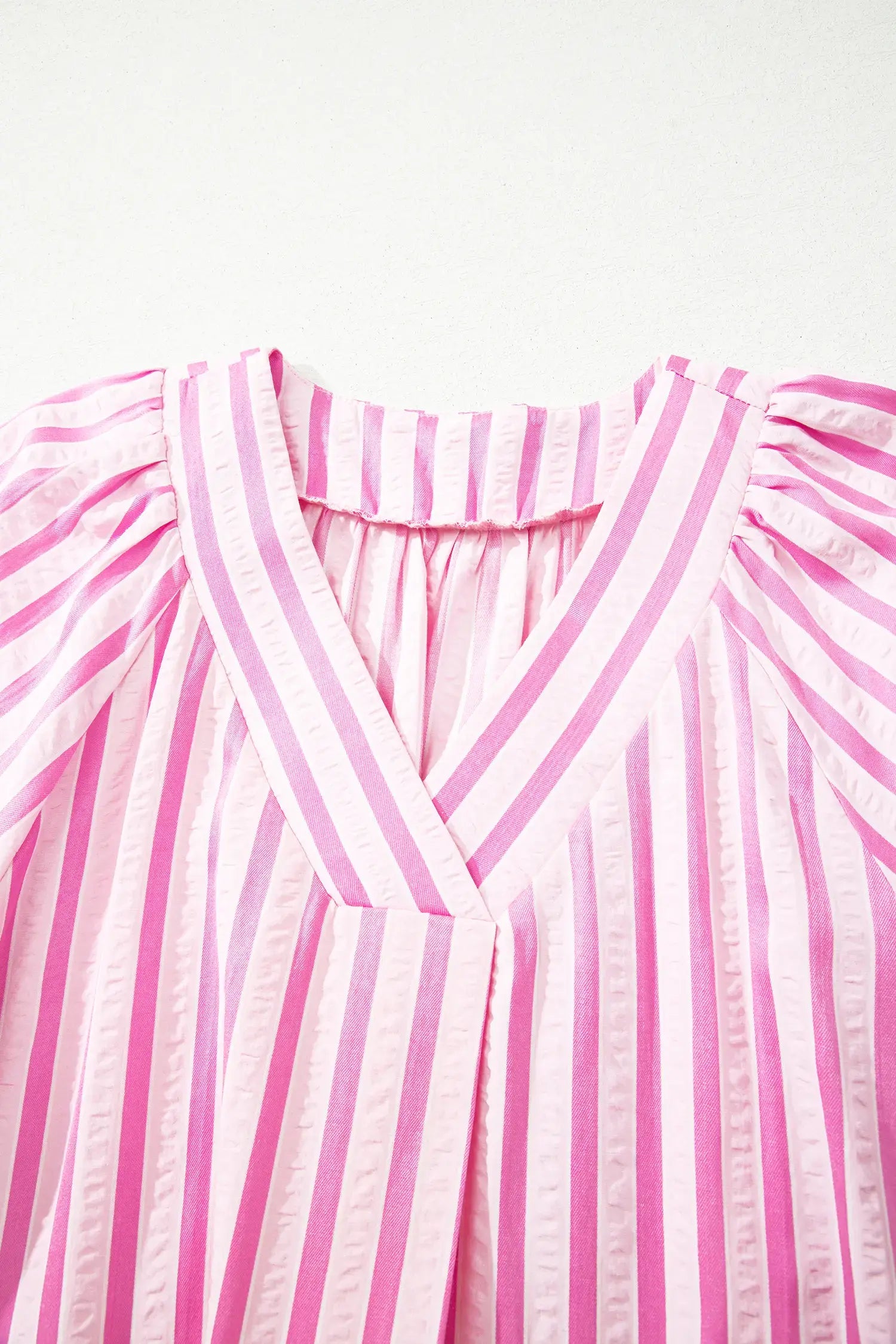 Pink and white vertically striped blouse with puffed shoulders and a gathered V-neckline, shown in a close-up studio shot against a plain light background.