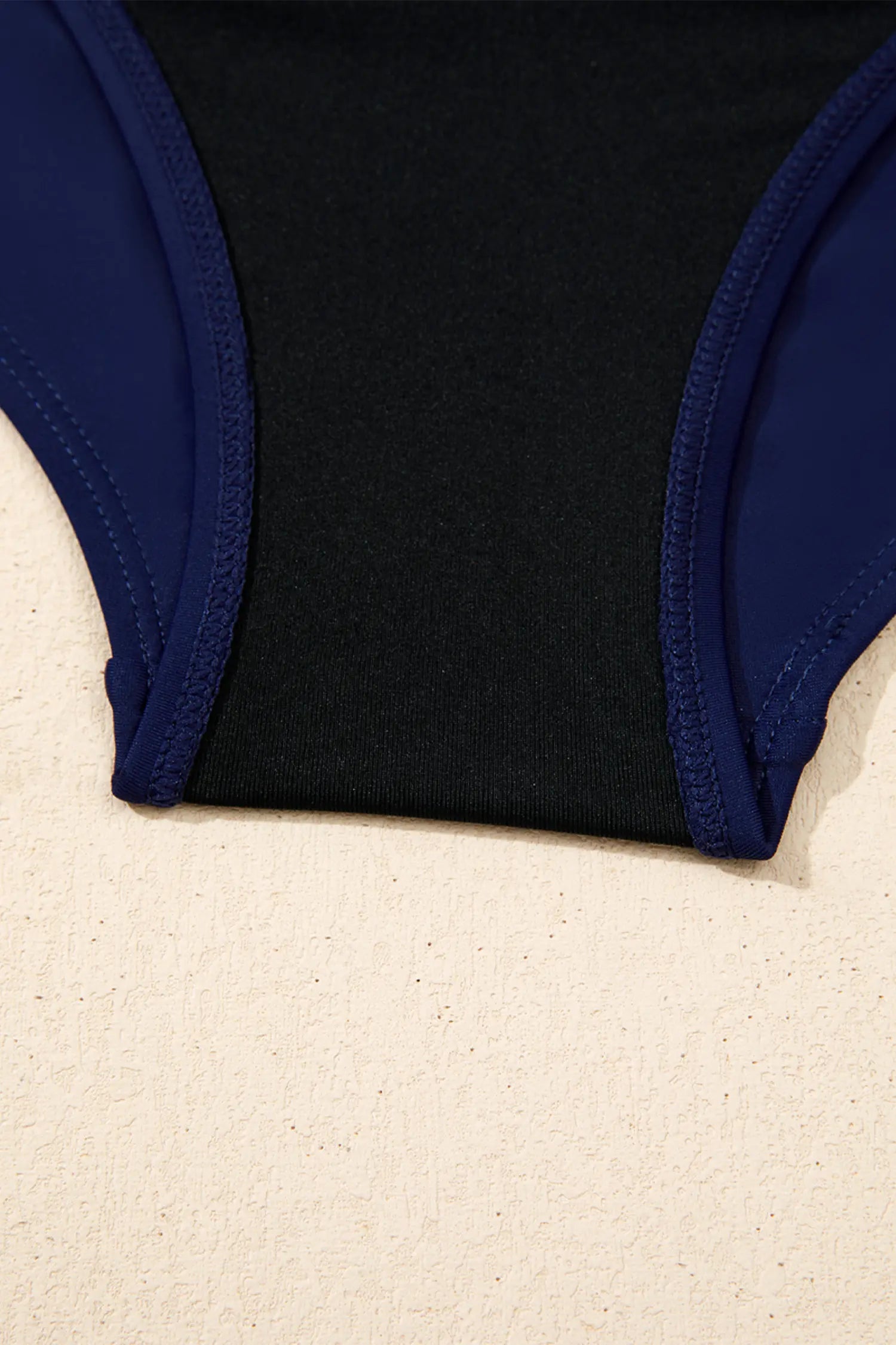 Black swimsuit bottom with blue trim on a beige surface