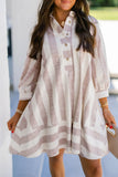 A woman wearing a loose, long-sleeve button-front dress with vertical blush pink and off-white stripes, photographed in a real outdoor/architectural setting.
