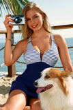 Woman in a striped swimsuit taking a selfie on a beach with a dog beside her.