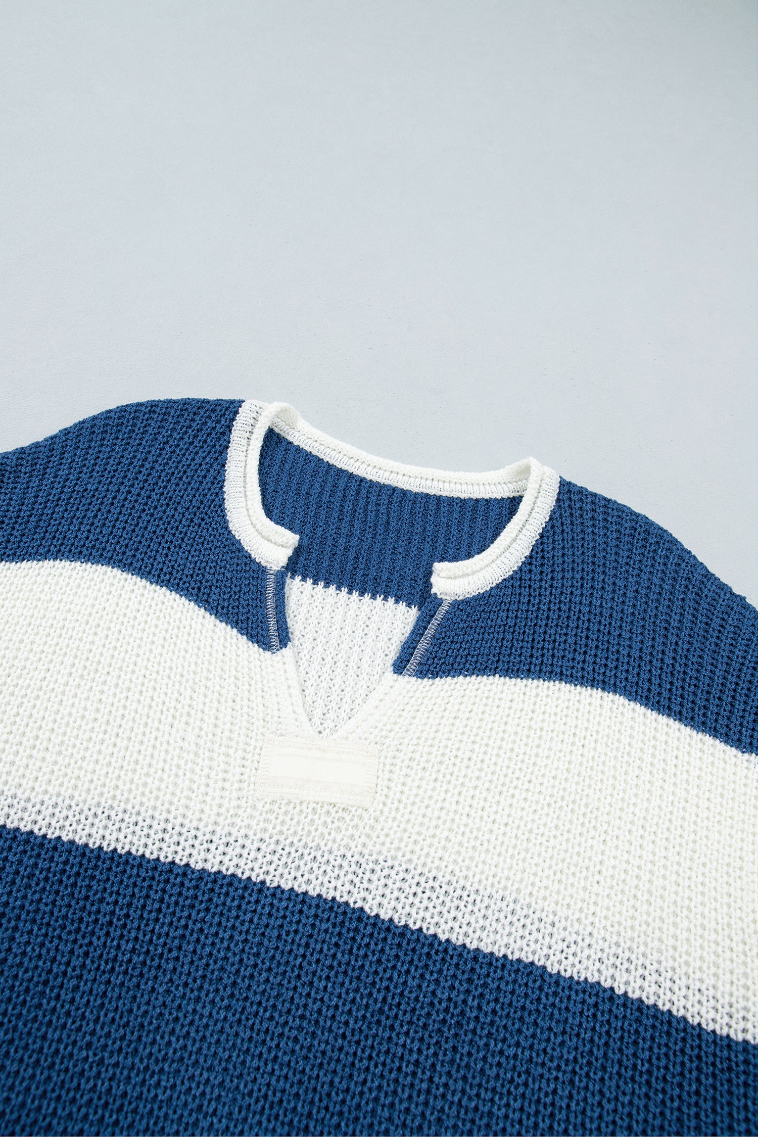 Close-up of a knitted sweater with horizontal stripes in deep blue and white, featuring a split neckline with white trim.