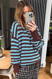 A woman takes a mirror selfie wearing a fuzzy knit sweater with horizontal light blue and dark brown stripes, paired with black and white plaid pants.