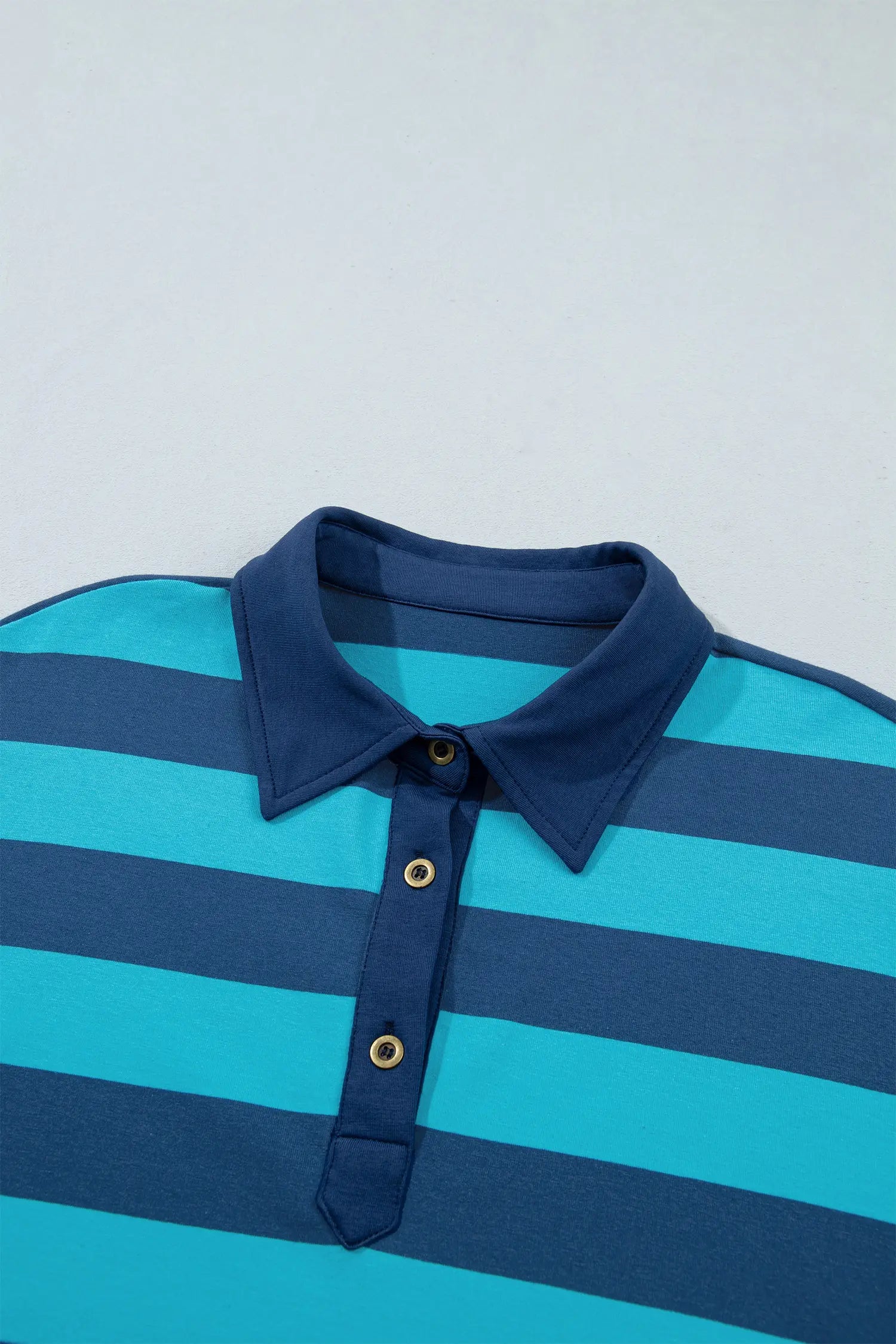 Close-up of navy-turquoise striped polo shirt with navy collar and gold buttons.
