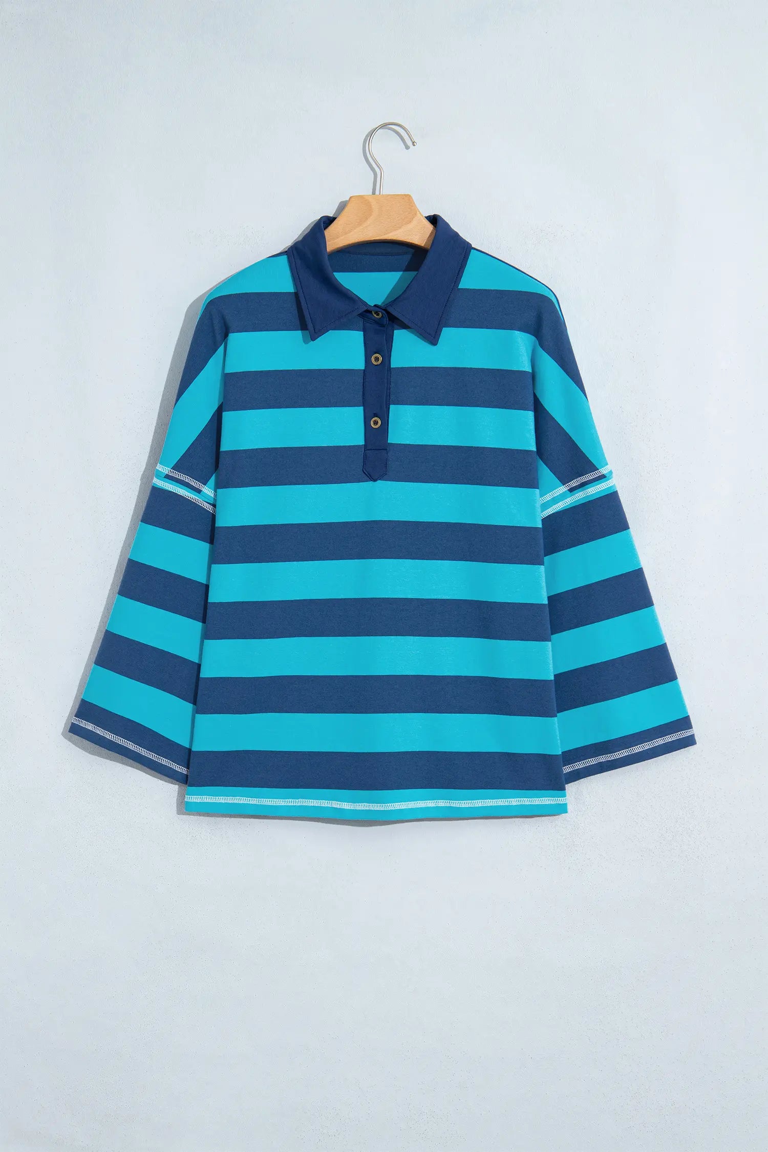 Navy blue and turquoise striped long-sleeve polo shirt on wooden hanger.