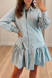 A woman wearing a light blue and white vertically striped button-up shirt dress with ruffled details, standing in a room with light wood floors.