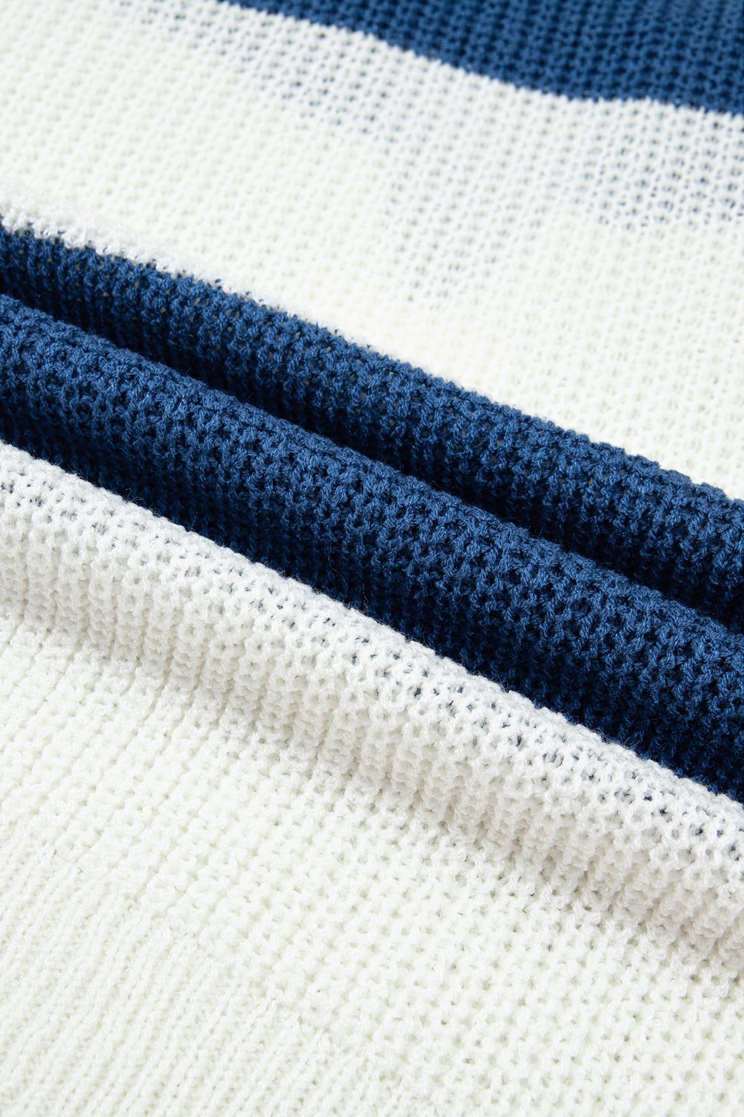 Close-up of a knitted fabric with alternating wide white stripes and two darker navy blue horizontal bands.