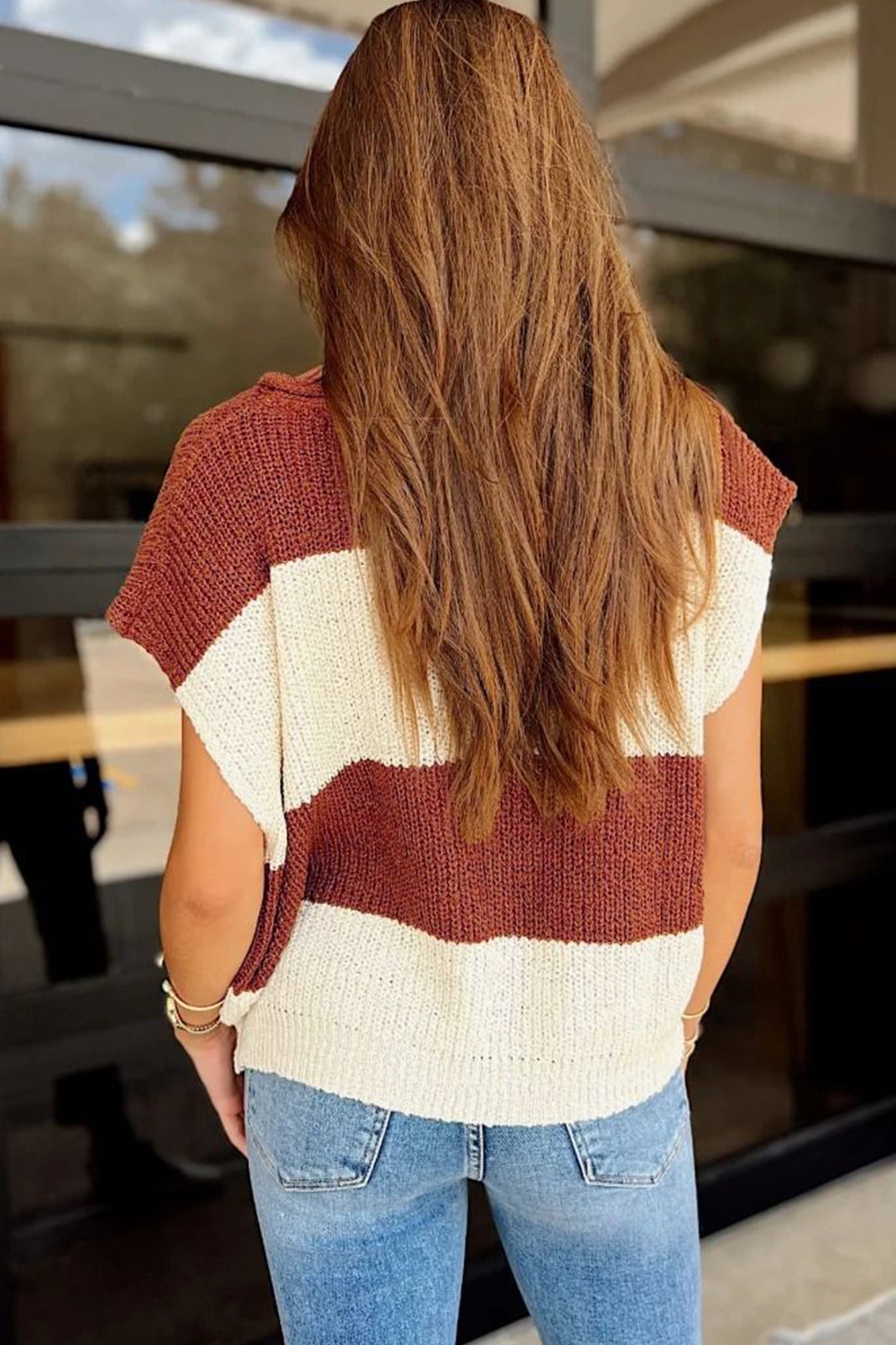 Woman from behind in a chunky rust brown and cream striped sweater with light blue jeans.