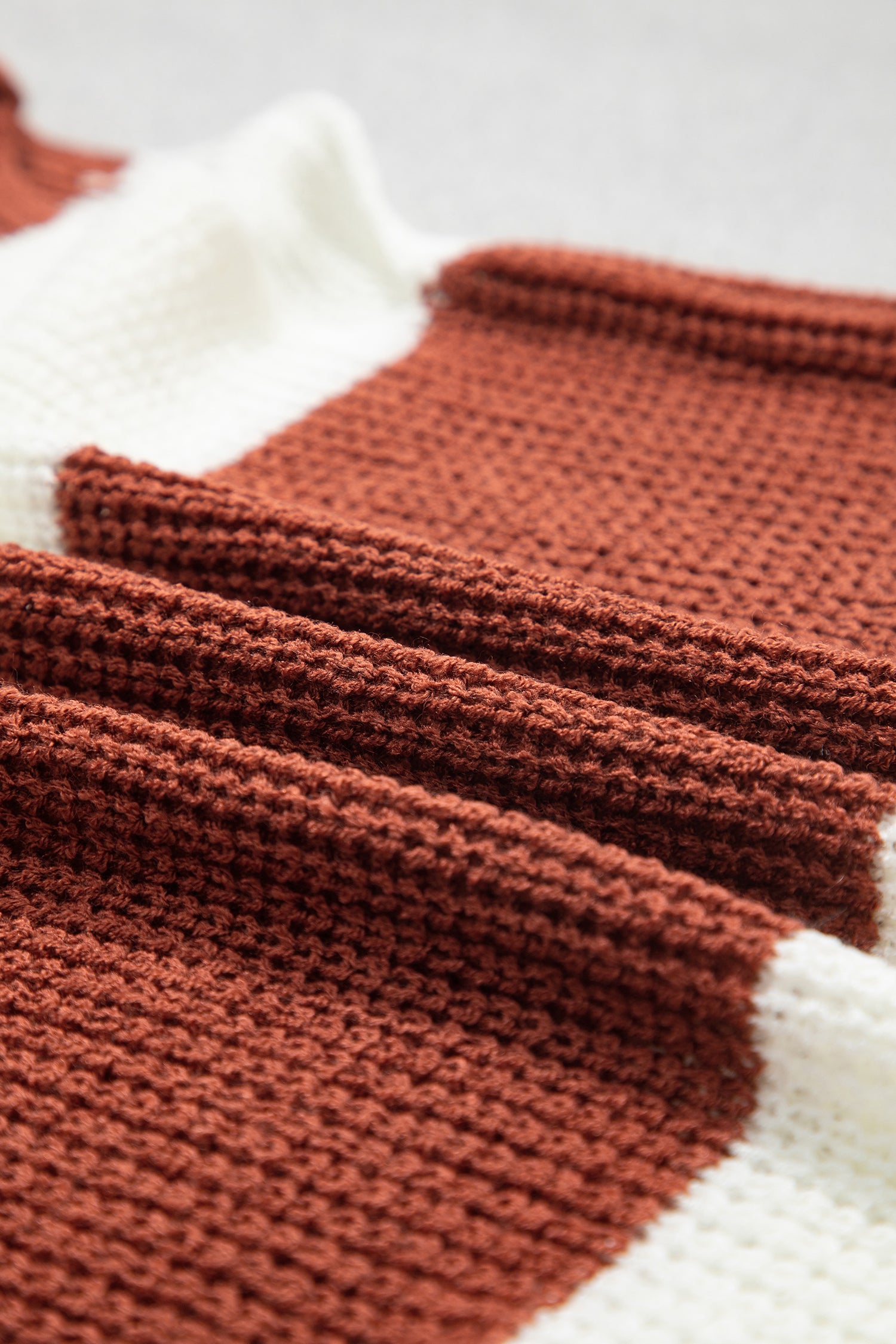 Close-up of a knitted textile with alternating wide bands of rust brown and off-white, showing the texture and stitch detail.