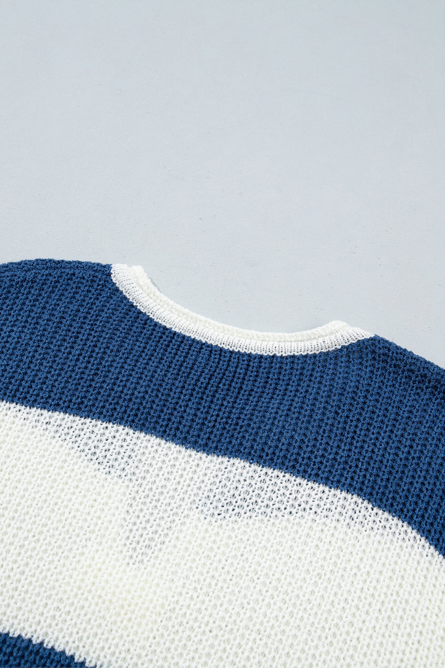 Close-up of a knit sweater showing a navy blue and white horizontal stripe pattern with a white ribbed crew neck.