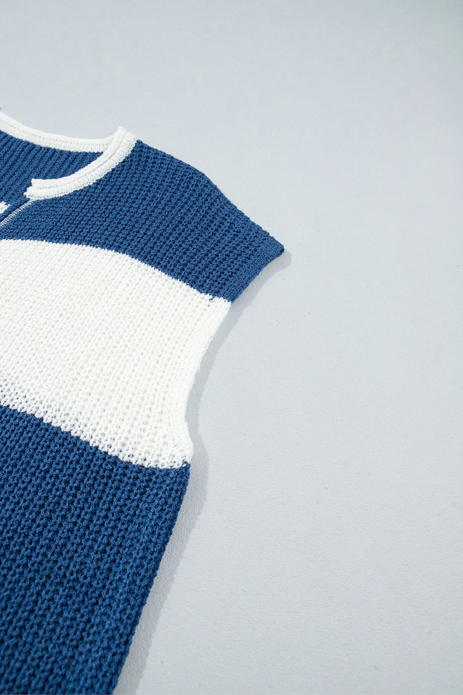 Close-up of a ribbed knit garment corner showing a white cuff with a curved hem and a dark blue textured section on a light gray background.