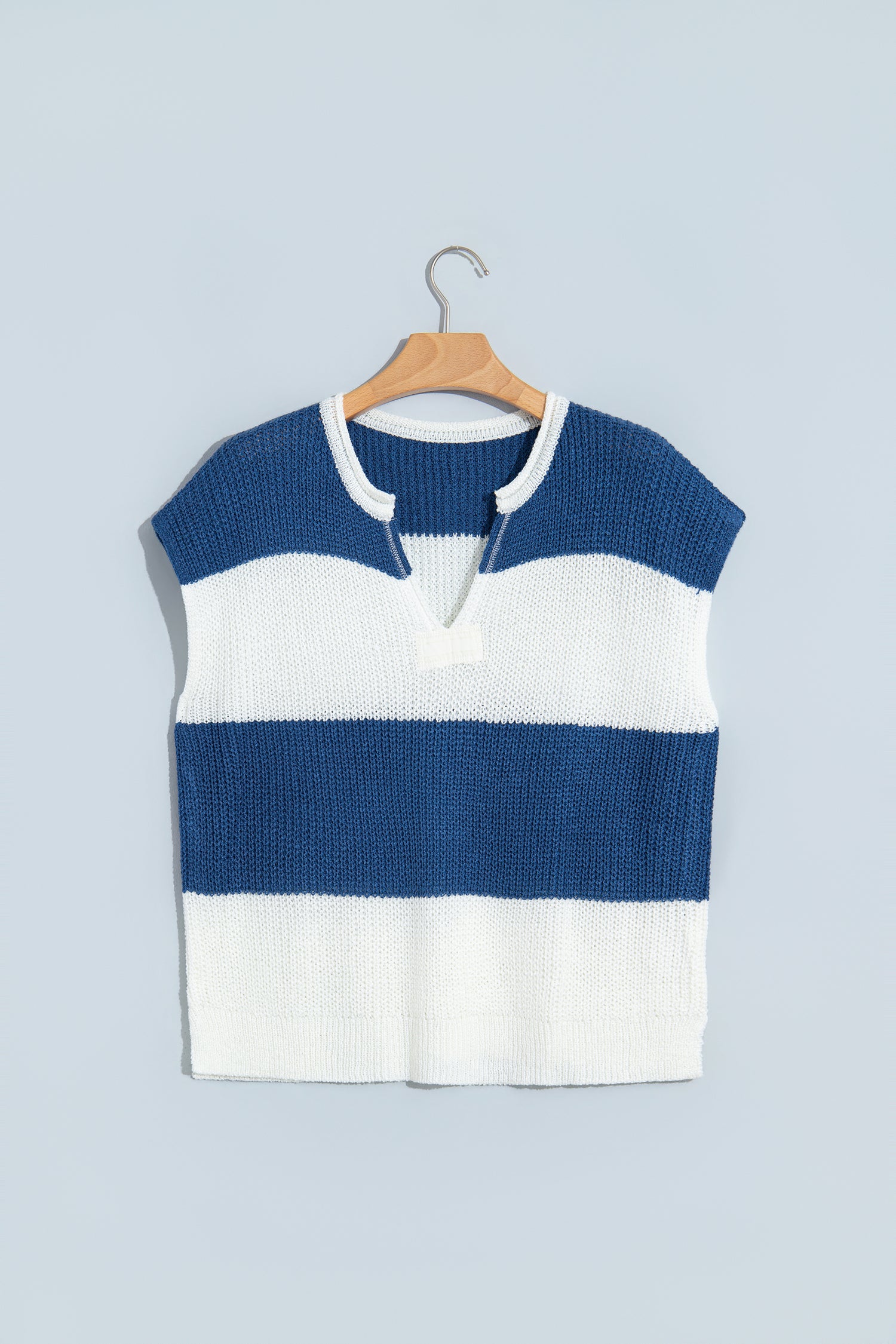 A sleeveless knit top with horizontal navy blue and white stripes, hanging on a wooden hanger against a light blue-gray background.