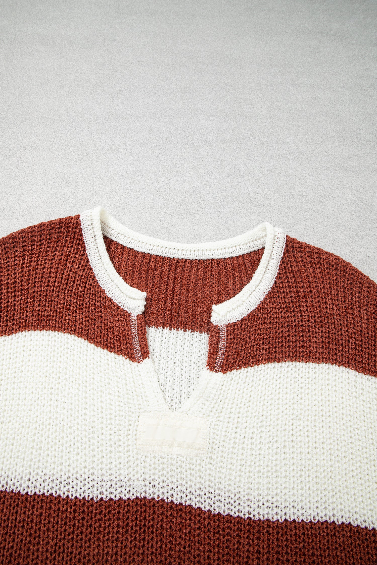 A close-up of a knit sweater with horizontal rust brown and off-white stripes, featuring a split neckline with white ribbed trim.