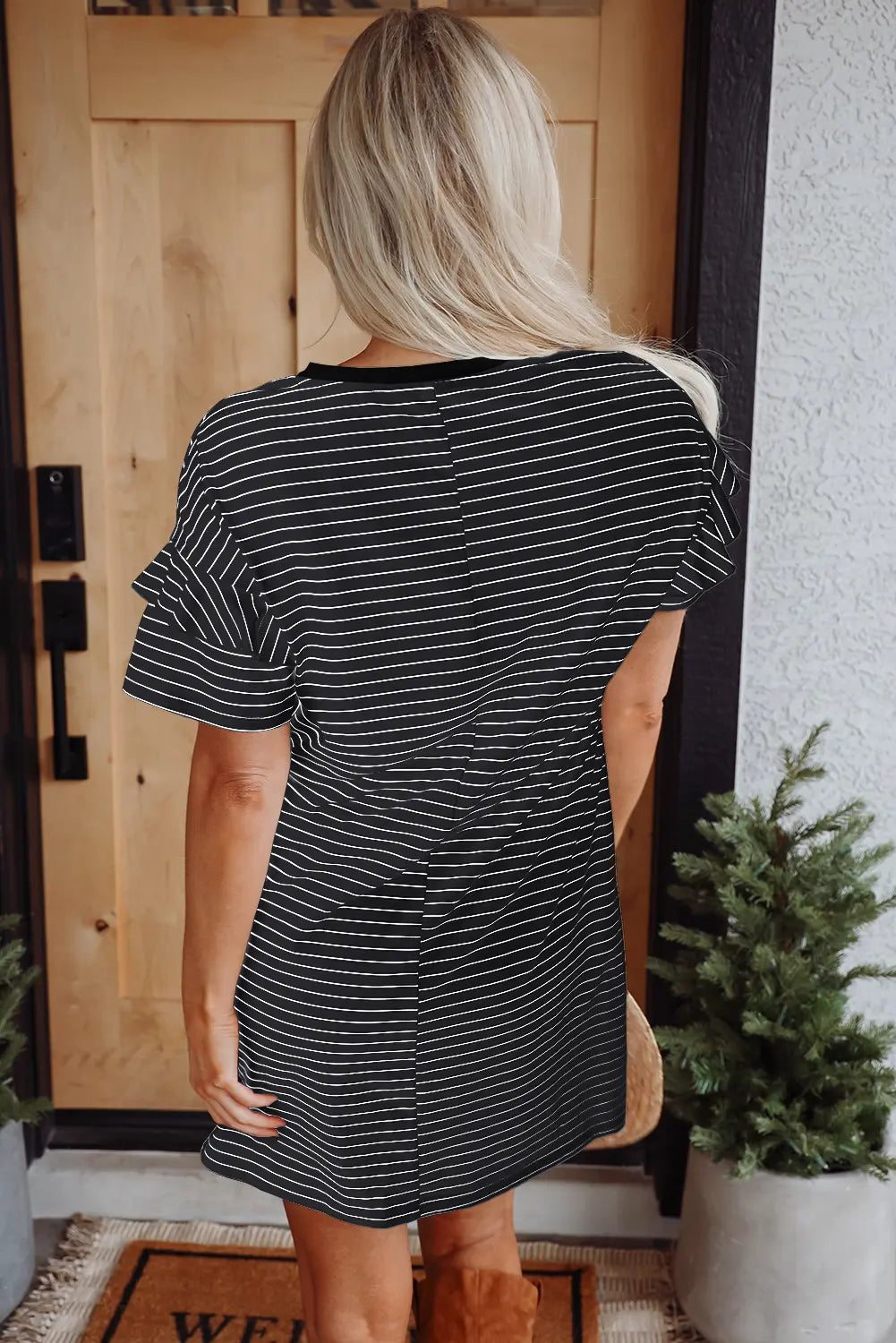Person wearing a black and white striped dress standing in front of a wooden door with a Christmas tree in the background.