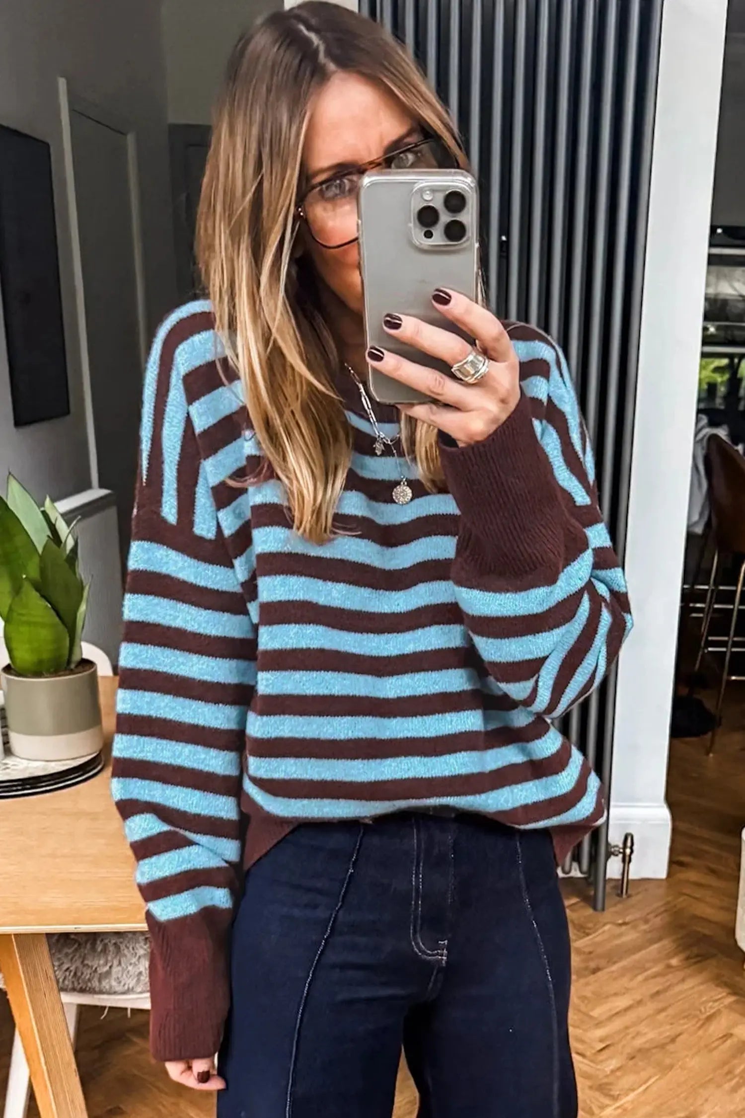 A woman takes a mirror selfie wearing a cozy knit sweater with horizontal stripes in light blue and dark brown, paired with dark blue jeans.