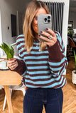 A woman takes a mirror selfie wearing a knit sweater with horizontal brown and light blue stripes, paired with dark blue jeans in a home interior setting.