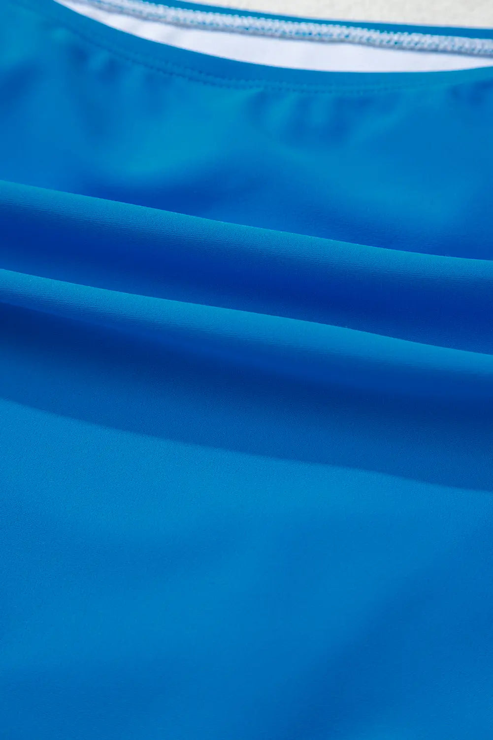 Close-up of a bright blue fabric garment, showing the texture and a sliver of a white inner collar.