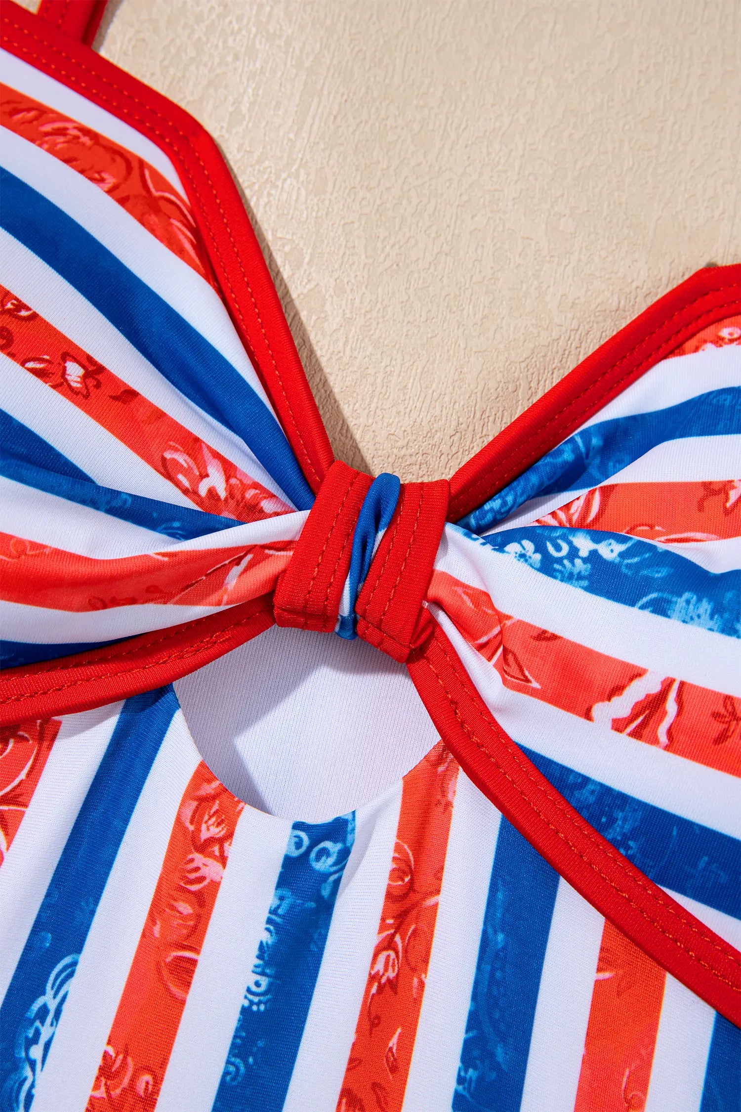 Close-up of a bikini top with red, white, and blue stripes on a beige background
