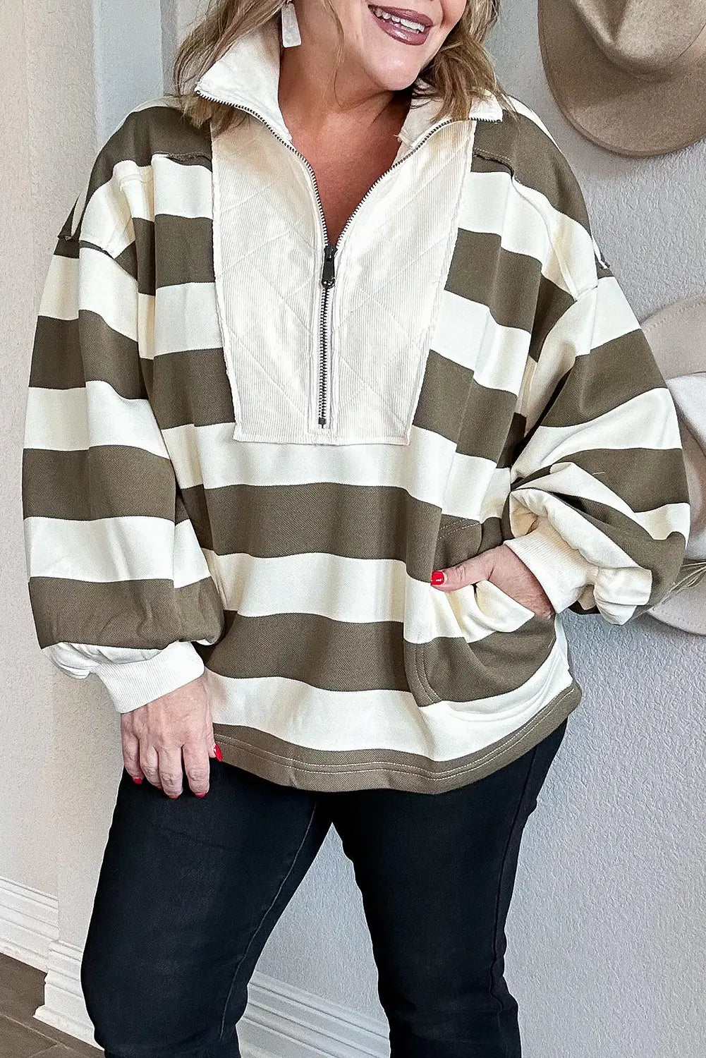 A woman wearing a cream and olive green horizontally striped quarter-zip pullover sweatshirt with a mock neck and front pockets, paired with black jeans.