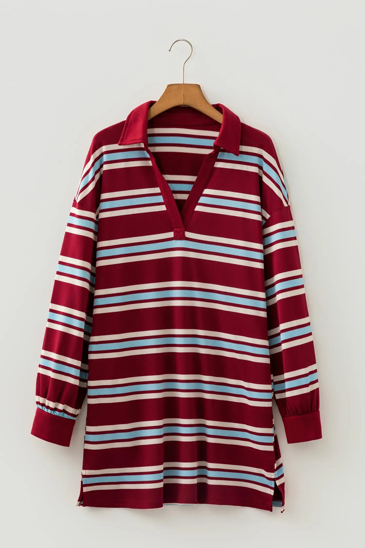 A long-sleeve collared knit top with horizontal stripes in burgundy, white, and light blue, hanging on a wooden hanger against a plain light gray wall.