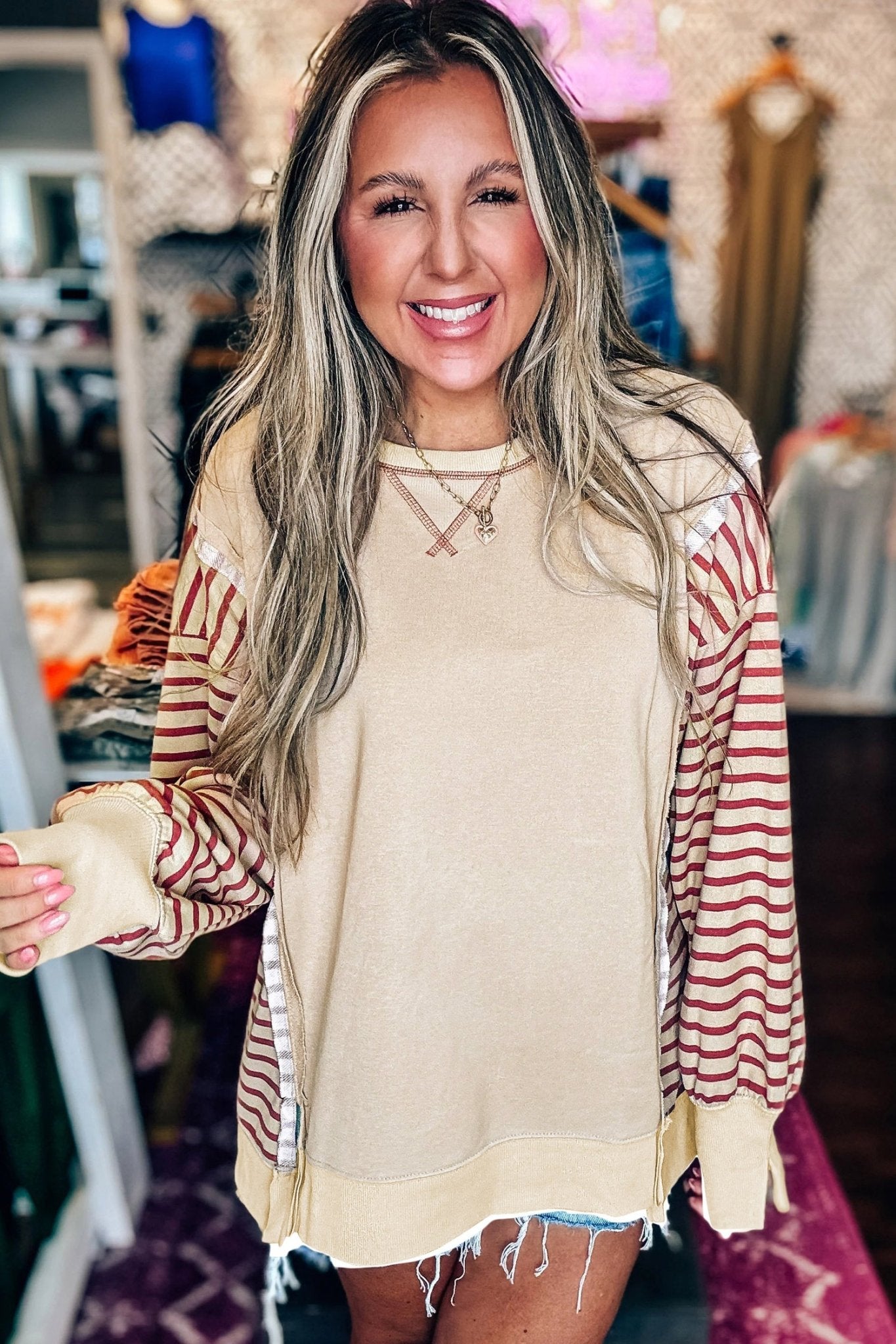 Woman wearing a beige sweater with striped sleeves in a store setting