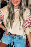 Woman wearing a beige top with red sleeves and denim shorts, smiling.