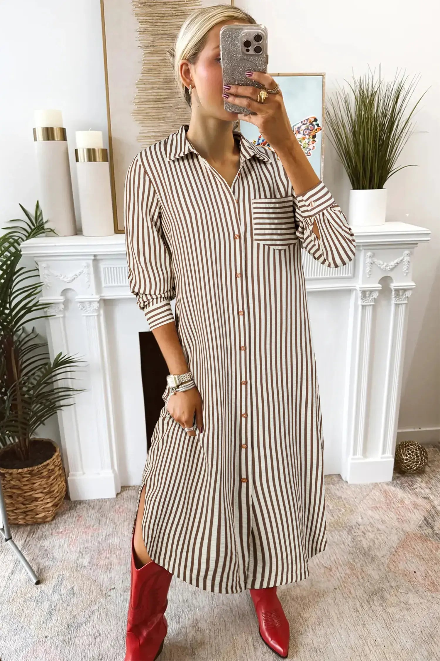 Woman taking a mirror selfie wearing a striped dress and red boots in a home setting.