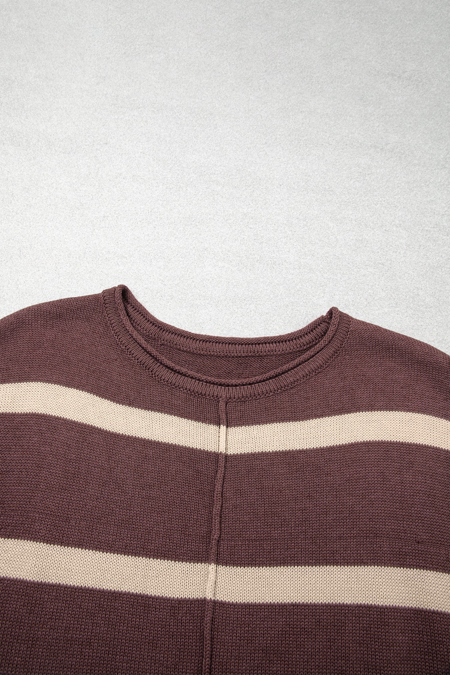 A close-up of a ribbed knit crewneck sweater with horizontal stripes in dark brown and cream, laid flat against a light gray background.