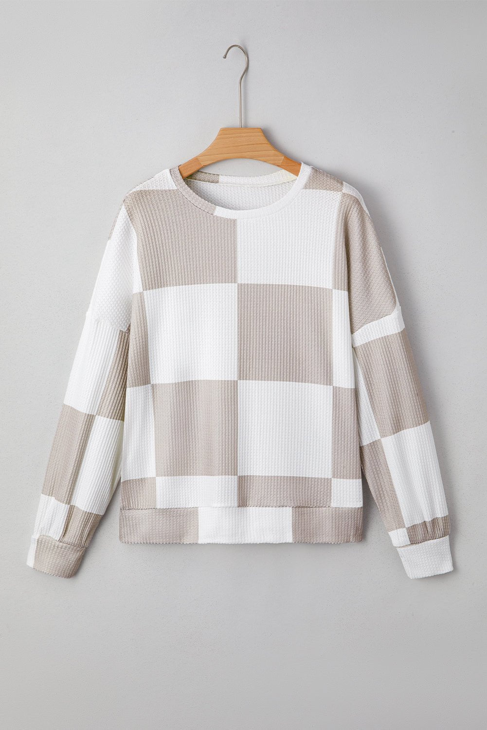 Checkered sweater on a hanger against a gray background