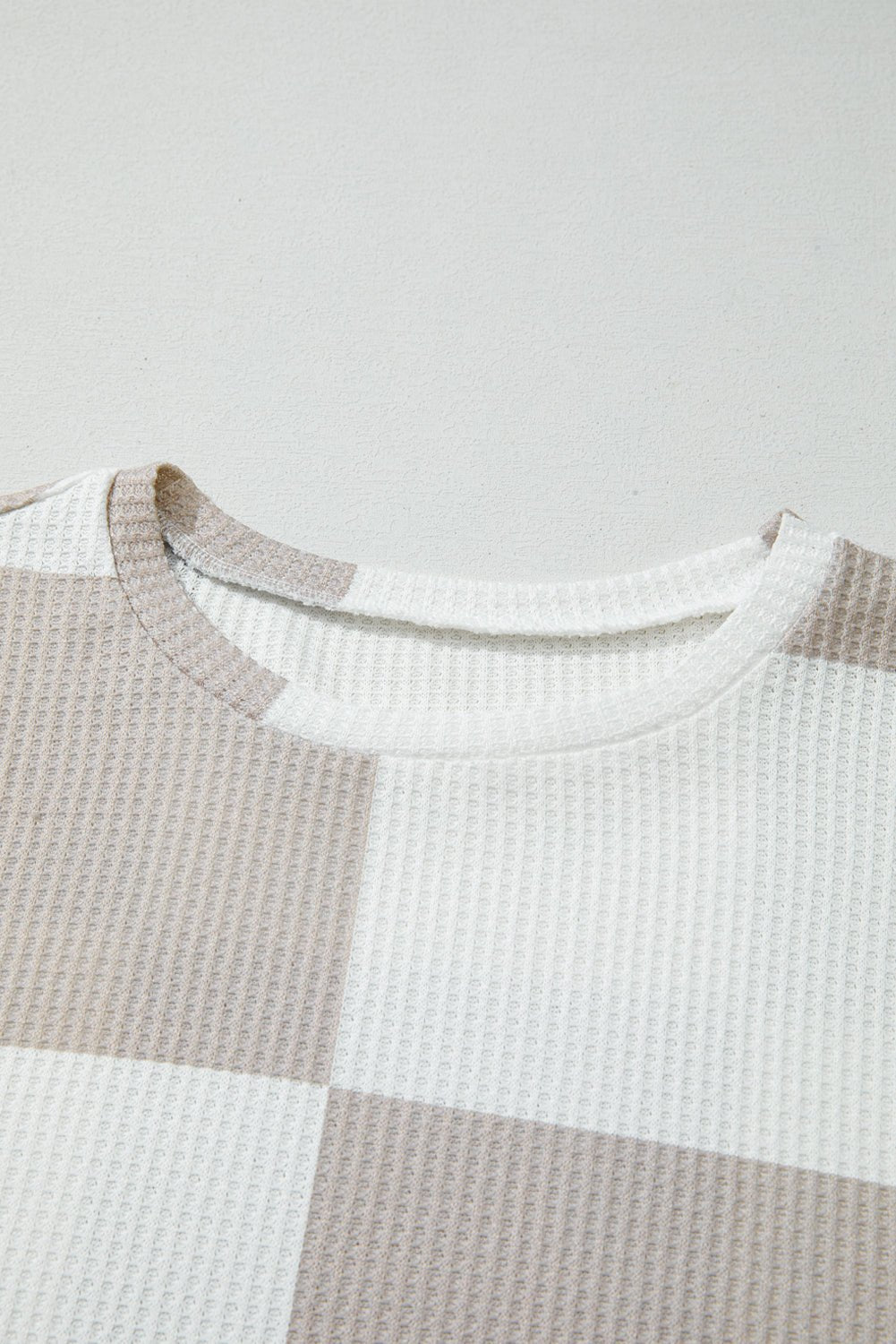 Close-up of a checkered shirt with brown, white, and gray pattern on a light gray background