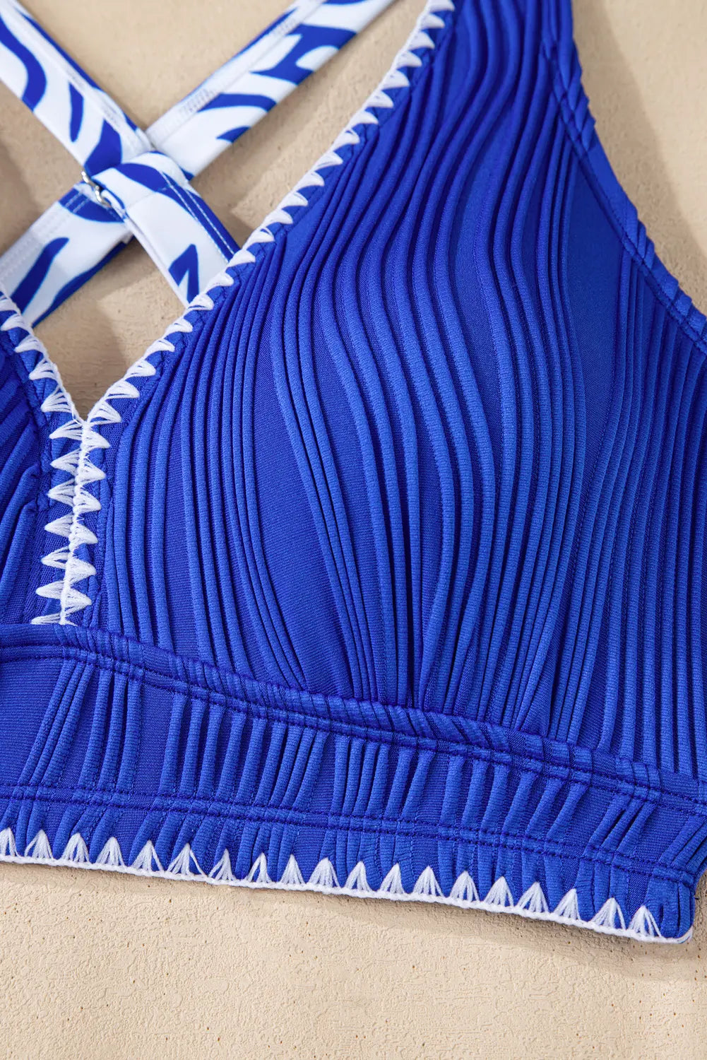 Blue bikini top with white trim on a beige background