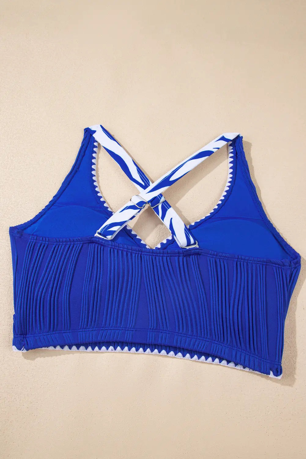 Blue bikini top with white and blue striped straps on a beige background