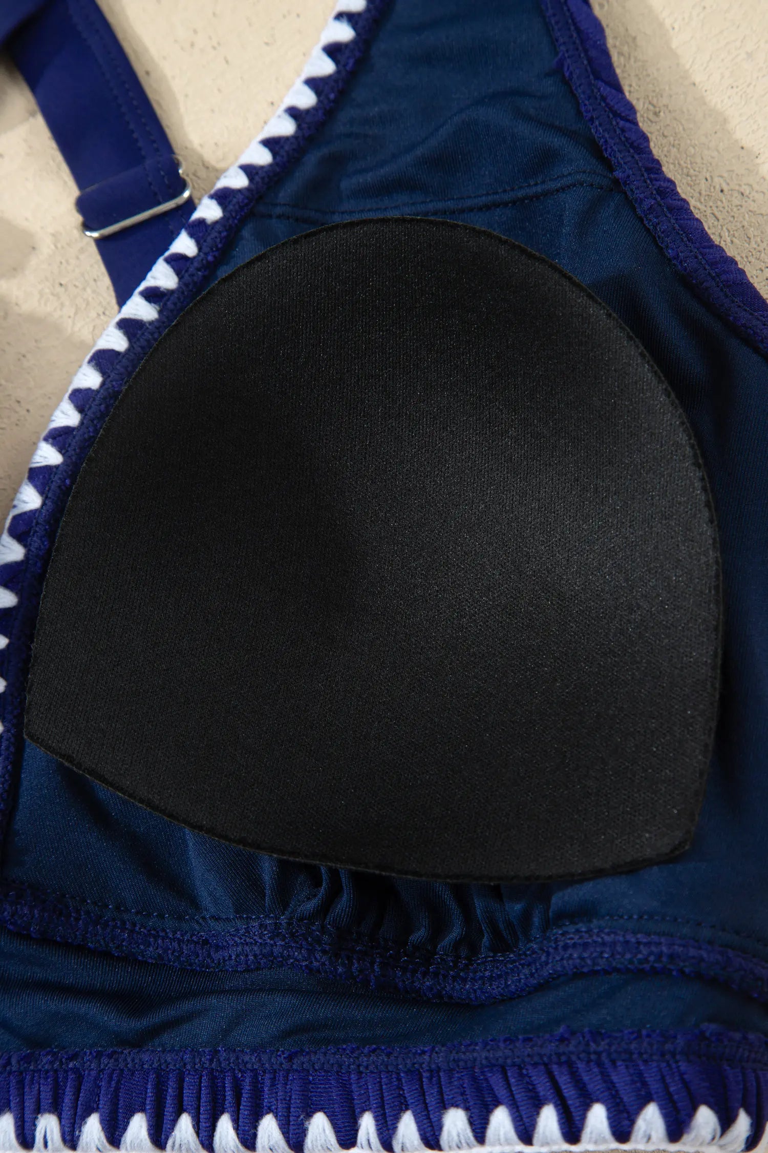 Close-up of a navy blue bralette with a black underwire pad and white zigzag trim along the edges.