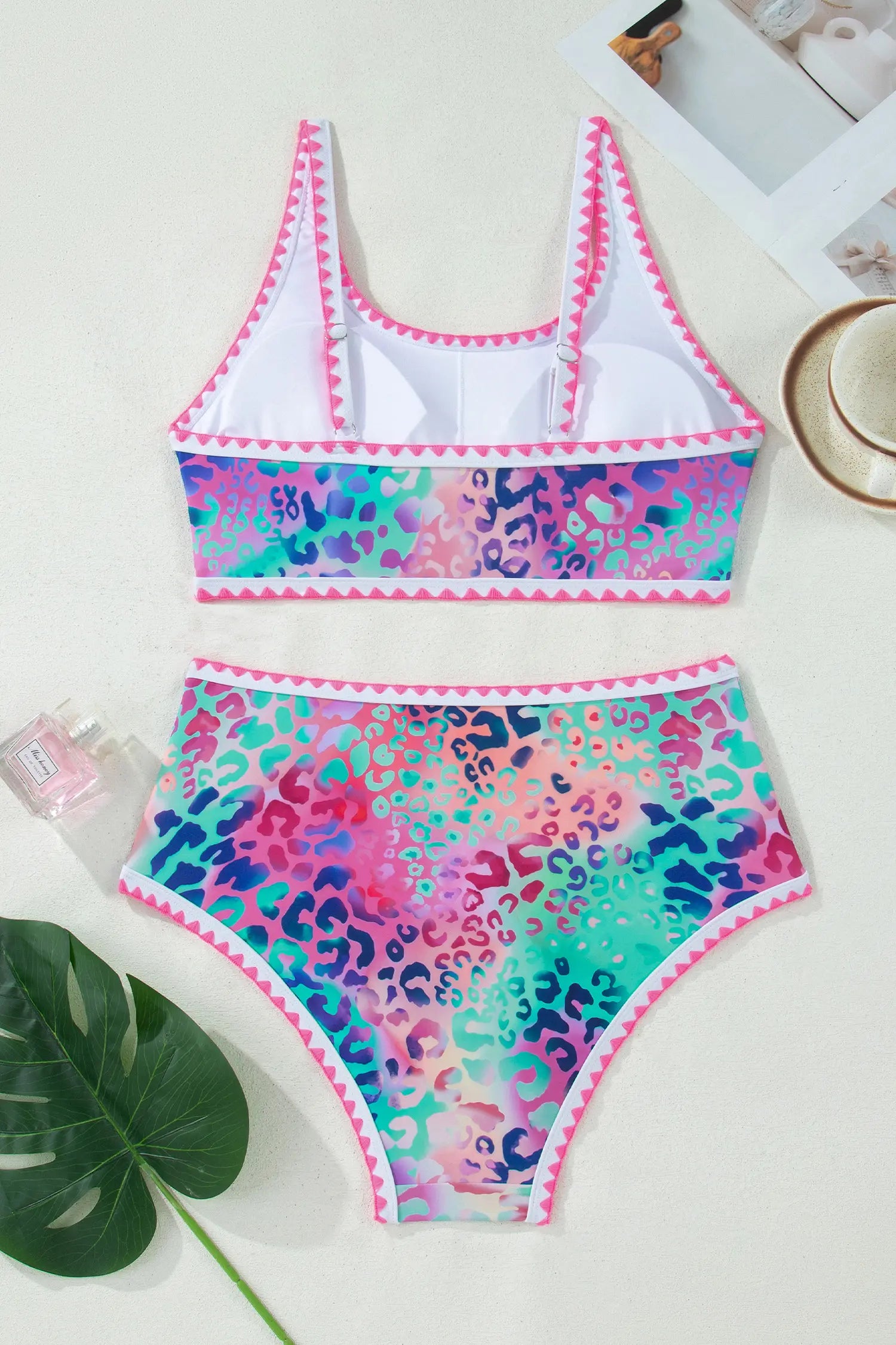 Colorful leopard print swimsuit on a white surface with a plant leaf in the corner.