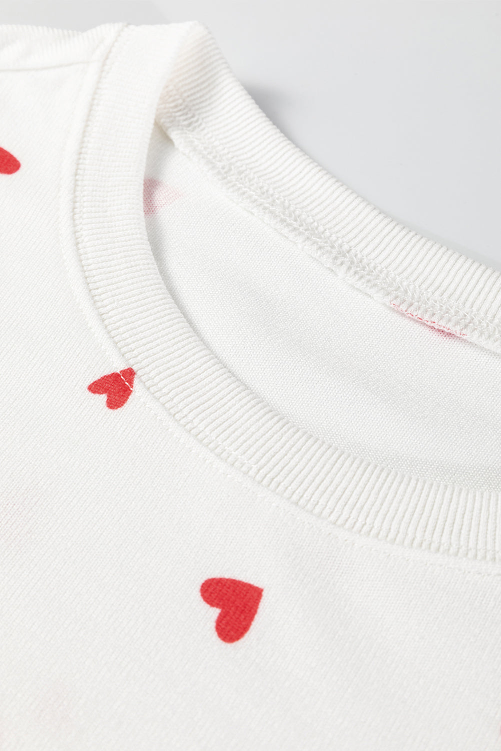 White sweater with red heart patterns on a light gray background