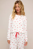 Woman wearing a white pajama set with red heart patterns on a beige background