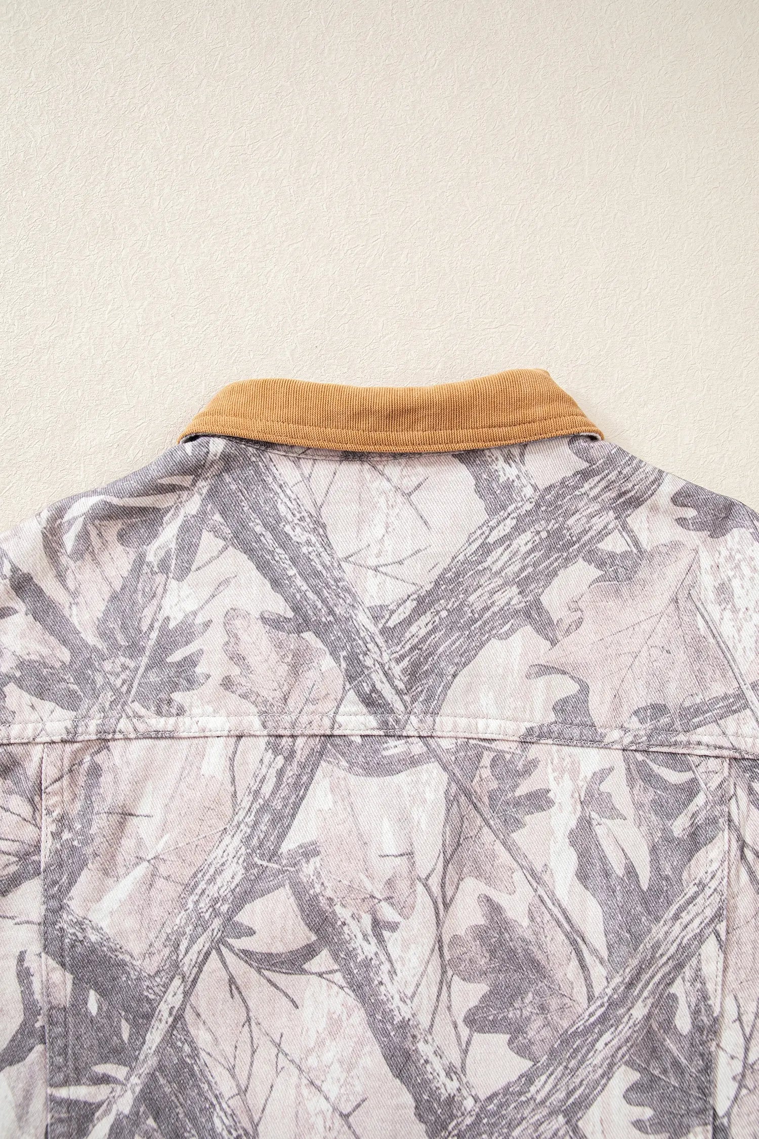 Close-up of camouflage shirt back collar with gray-beige woodland leaf print and contrasting tan collar.