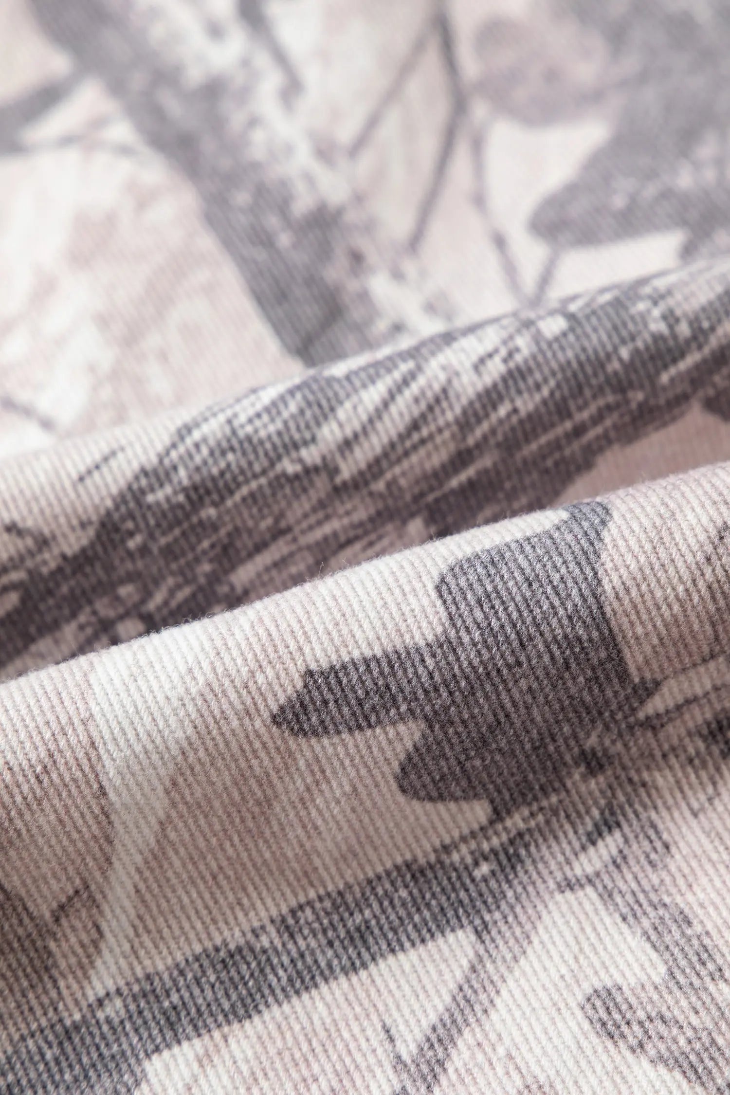 A close-up of draped fabric with a muted tree-bark camouflage pattern in gray, taupe, and off-white.