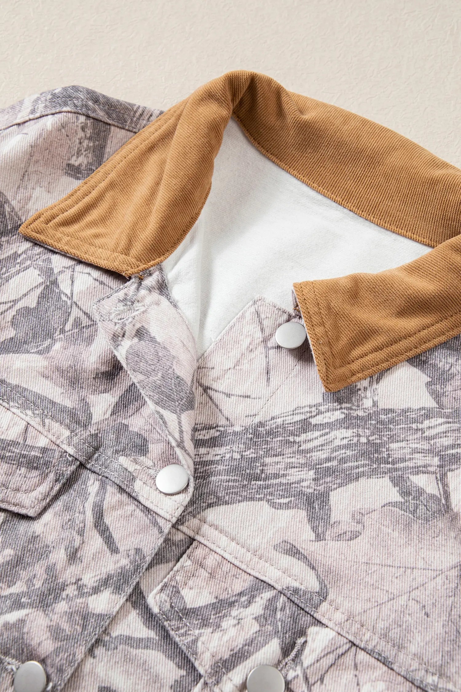 Close-up of gray-beige camouflage jacket with tan corduroy collar and white snap buttons.
