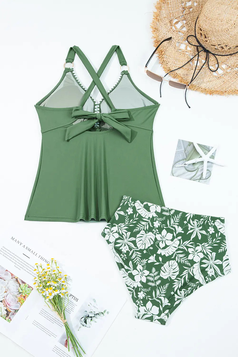 Green swimsuit with floral pattern, sun hat, and magazine on a light background