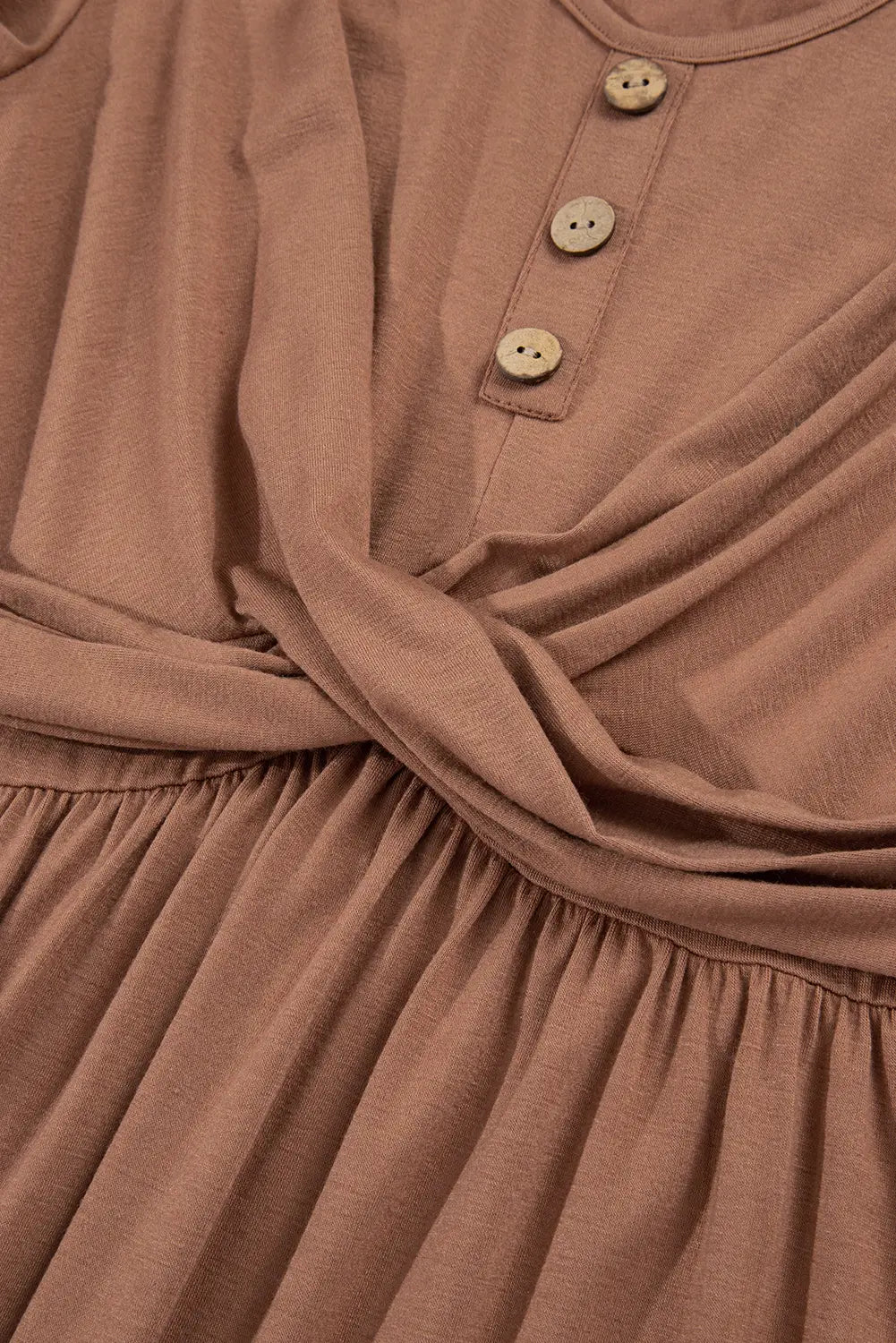 Close-up of a dusty rose or mauve-colored dress with a gathered waist, three-quarter sleeves, and a buttoned henley-style neckline.