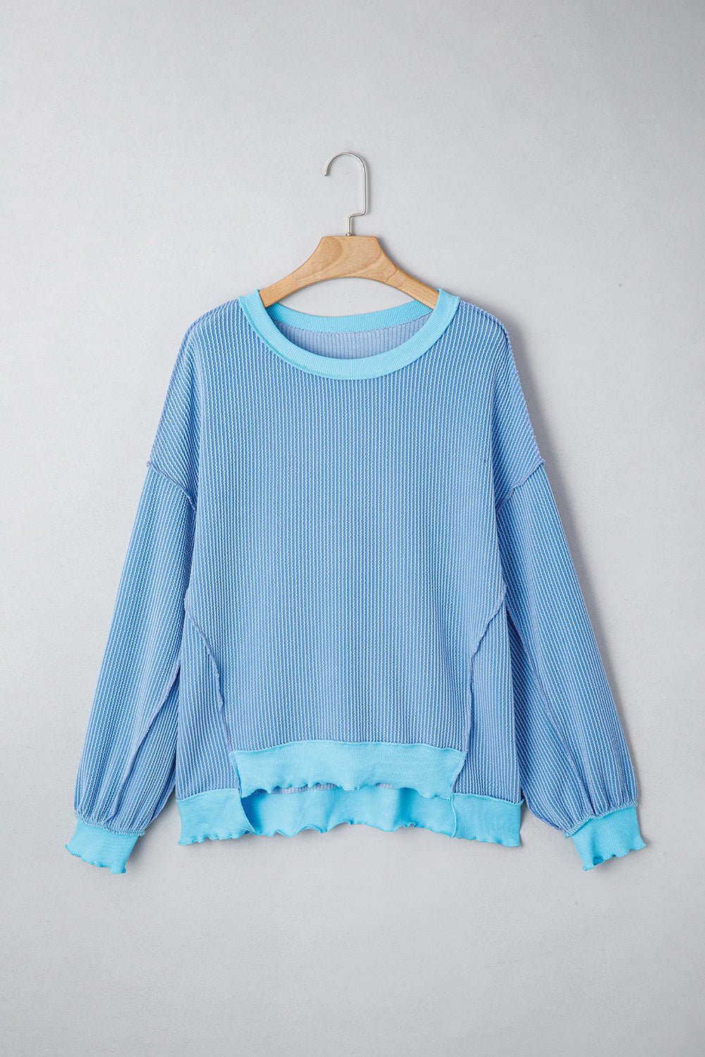 Blue ribbed sweater on a wooden hanger against a gray background