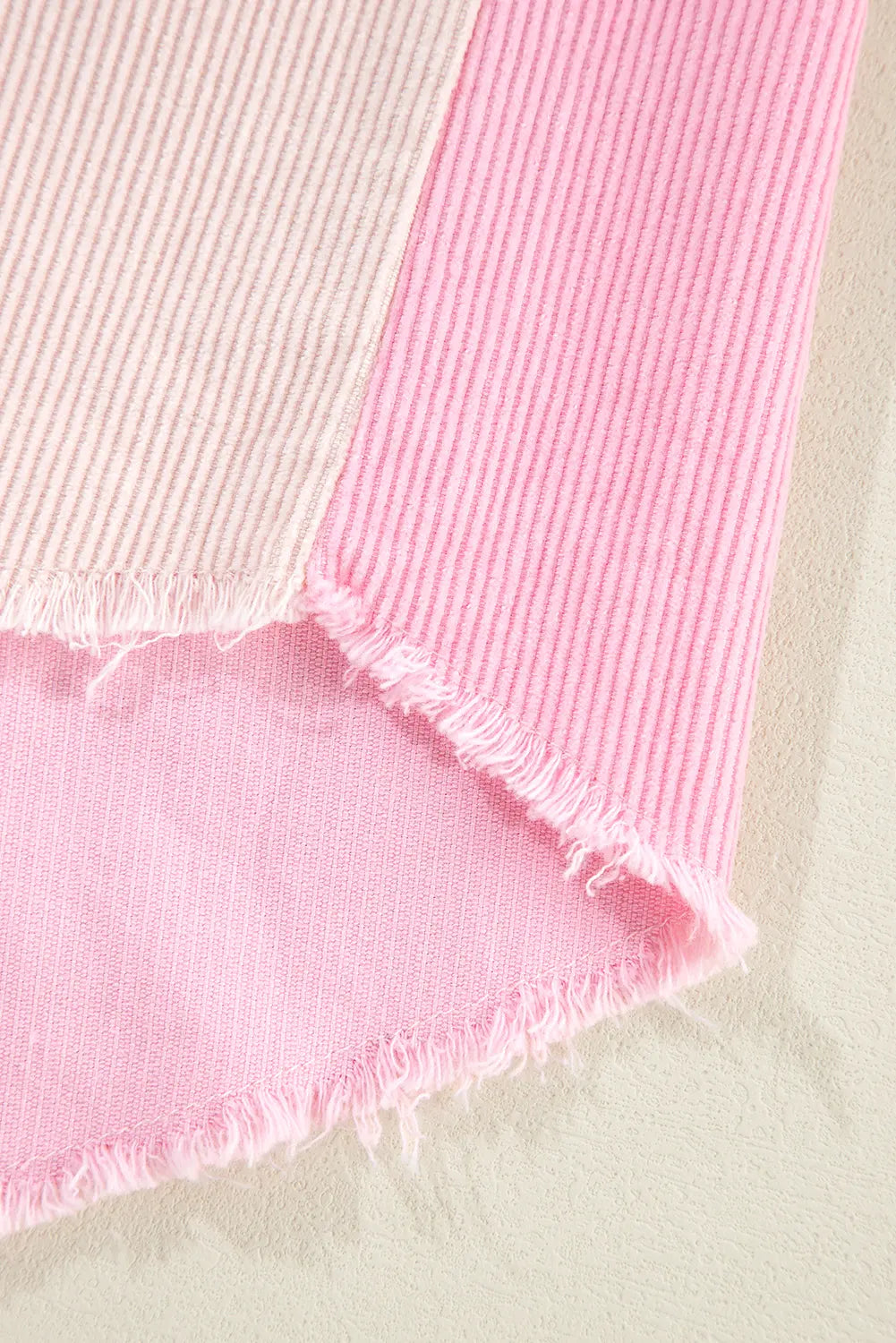 A close-up of a pink ribbed knit fabric with a frayed hem, laid diagonally on a light beige textured surface.