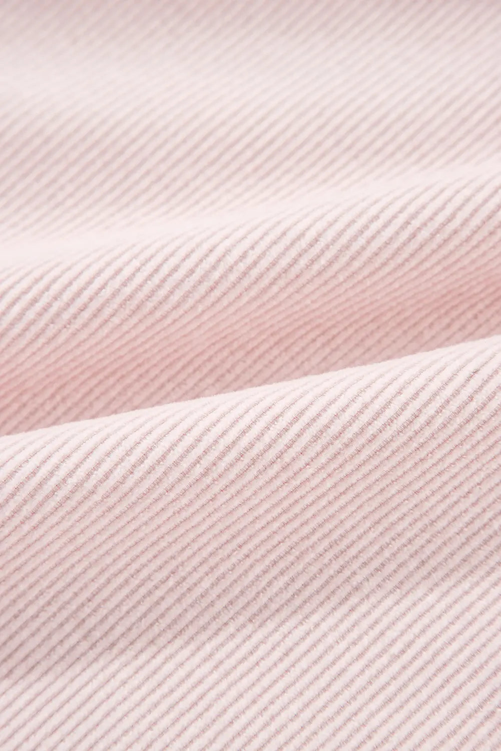 A close-up of light pink ribbed fabric with a fine diagonal texture and soft folds.