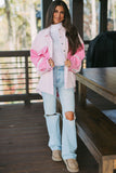 Woman wearing a pink and white jacket with ripped jeans on a wooden deck.