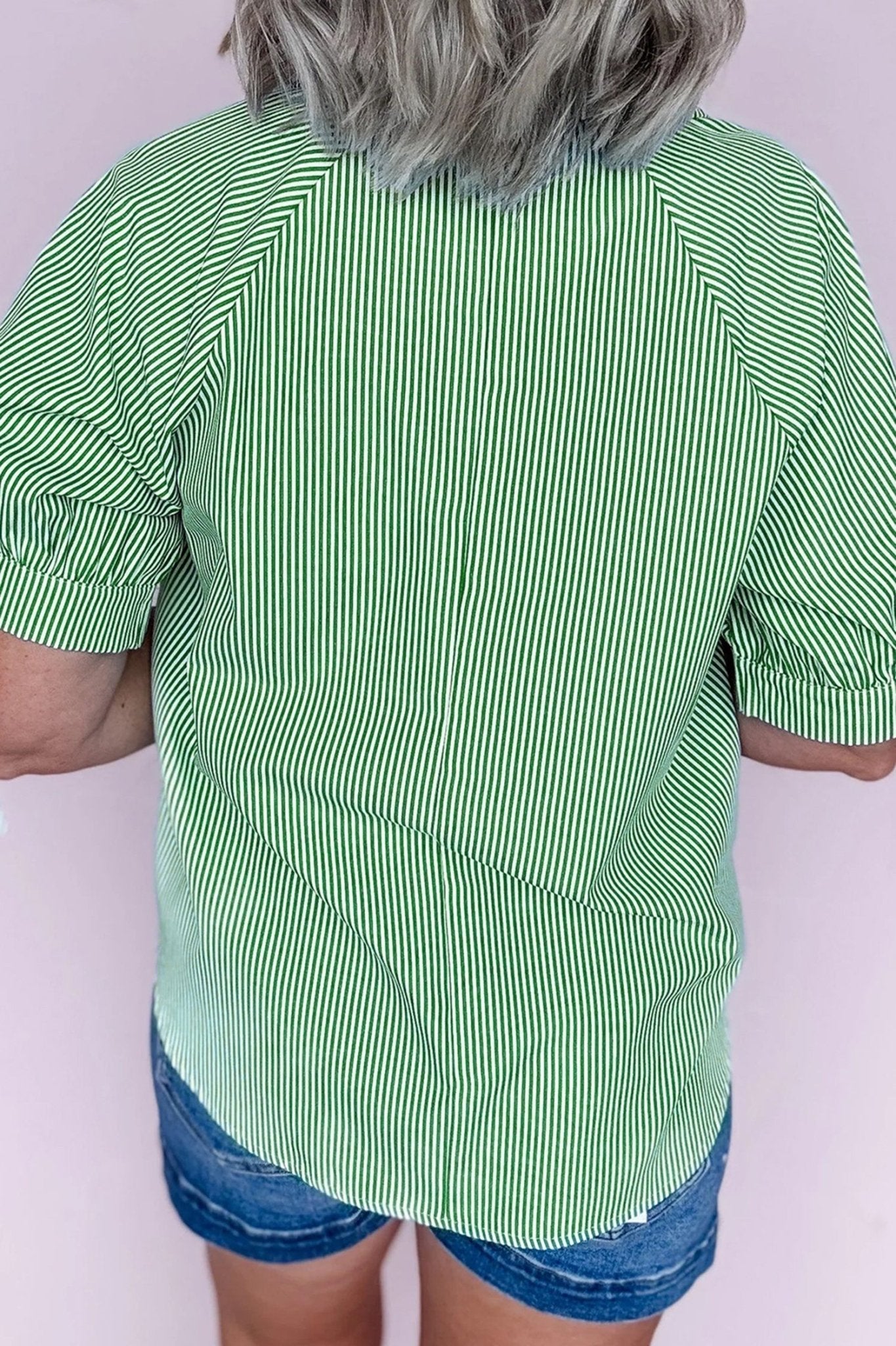 Person wearing a green and white striped shirt with blue shorts on a white background