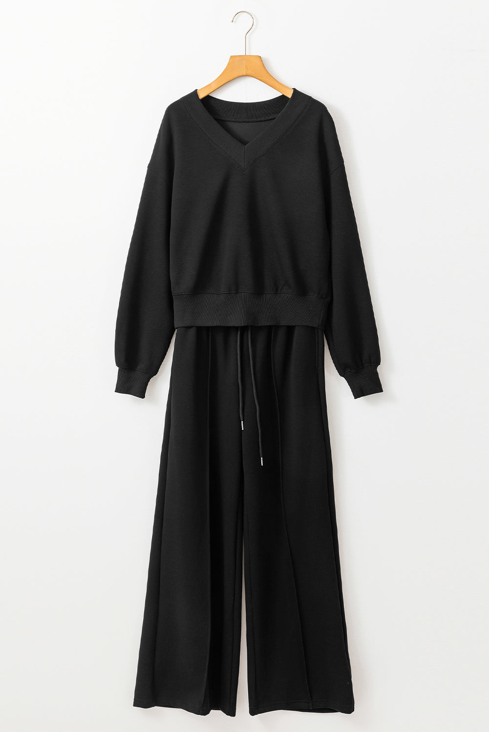 Black outfit with a top and pants on a hanger against a white background