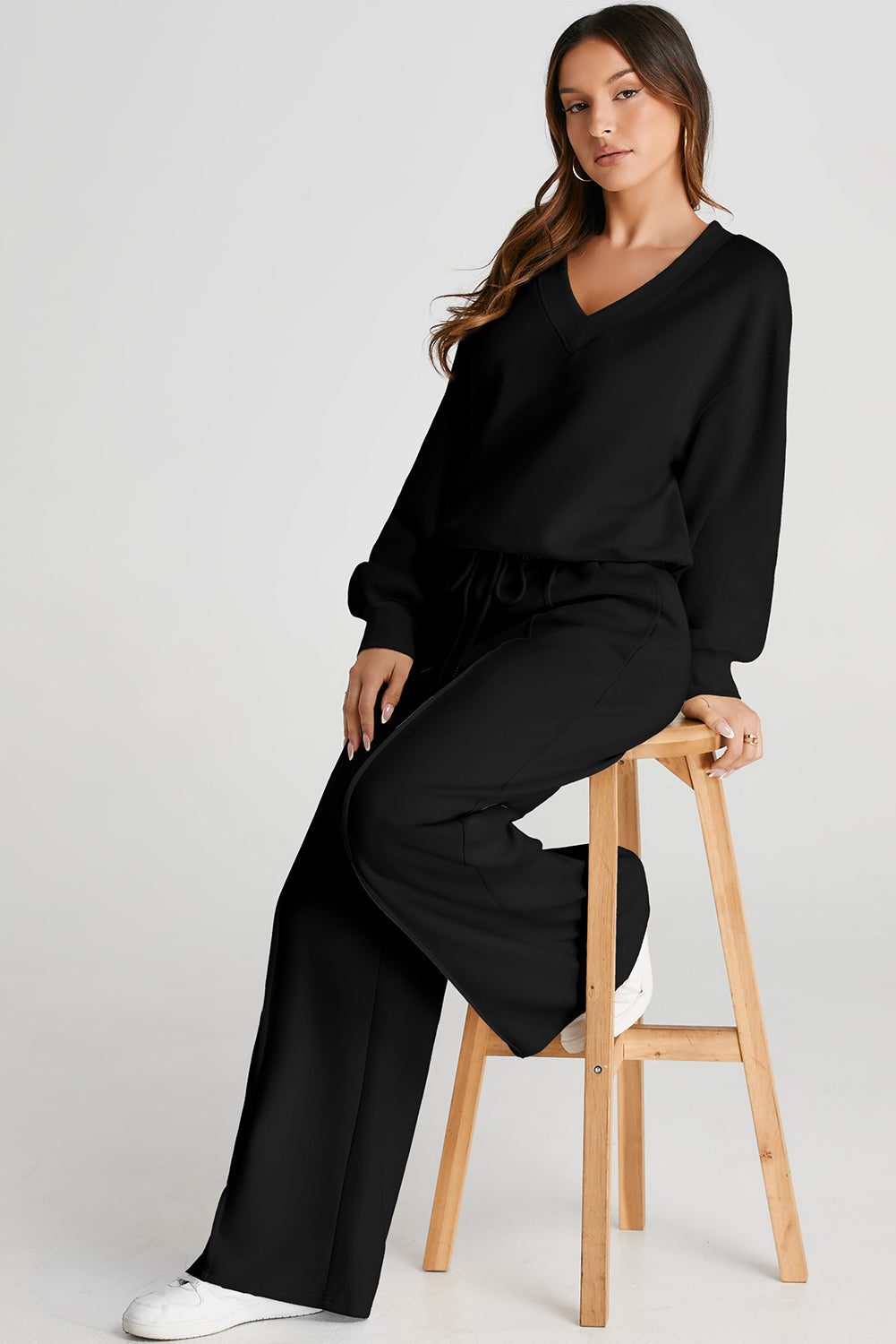 Woman sitting on a wooden stool wearing a black outfit against a white background